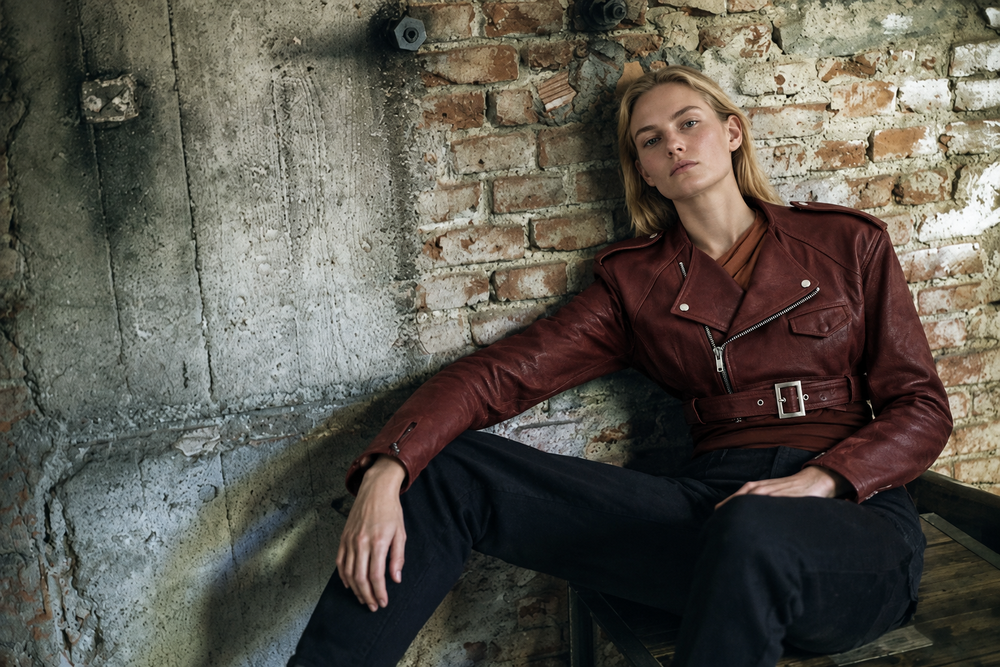 Woman model wearing Rick Owens leather jacket in seated brick-wall pose